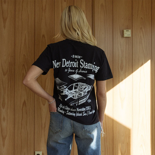 Woman with her back turned wearing the 8 Mile New Detroit Stamping T-Shirt, showcasing intricate prints of automotive parts and the legacy of Detroit's industry - Eminem Detroit Series.