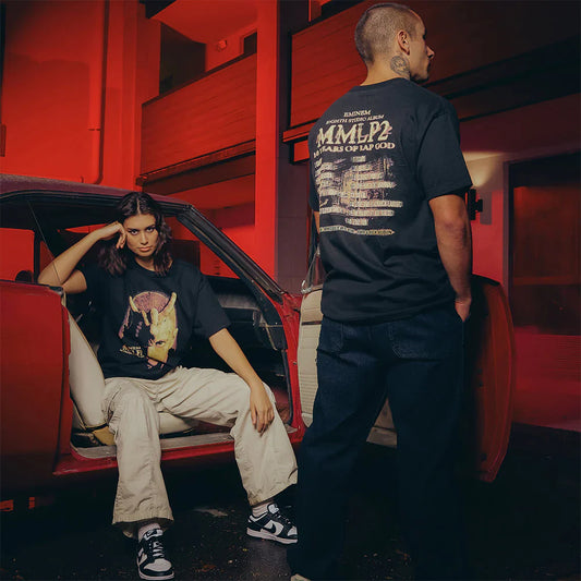 Male and female models by a red car, male model's back to the camera showing Eminem MMLP2 Horns T-Shirt with '10 Years of Rap God' tracklist.