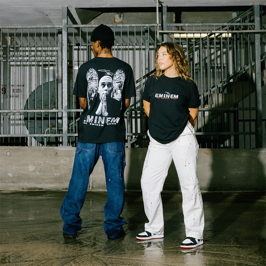 Male and female models posing in an urban setting, the male's back to the camera showing the stained glass graphic of the Eminem Show 20th Anniversary T-Shirt.