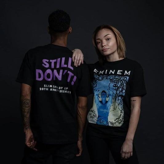 Two models posing together, one wearing the 'Still Don't' black T-shirt with the Slim Shady LP 20th Anniversary slogan on the back and the other wearing a graphic Eminem print on the front.