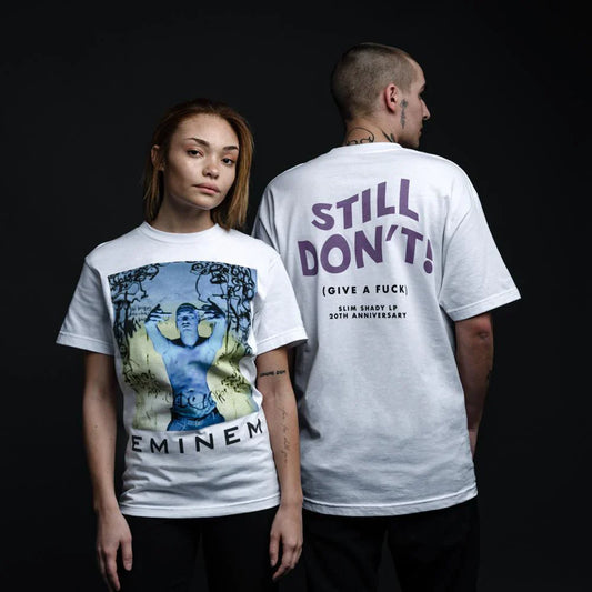 Male and female models facing away from each other, showcasing the front and back of the 'Still Don't Give A Fuck' Eminem white t-shirt, marking the Slim Shady LP's 20th anniversary.
