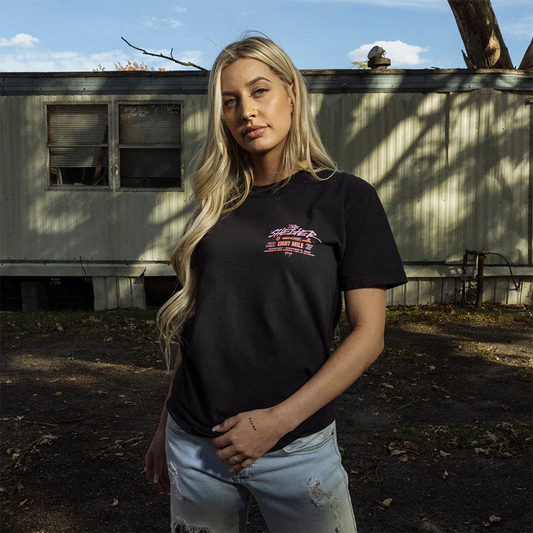 Woman posing in The Shelter Event Black T-Shirt, featuring a small logo with 'Shelter' text on the front - Eminem’s iconic venue merchandise.